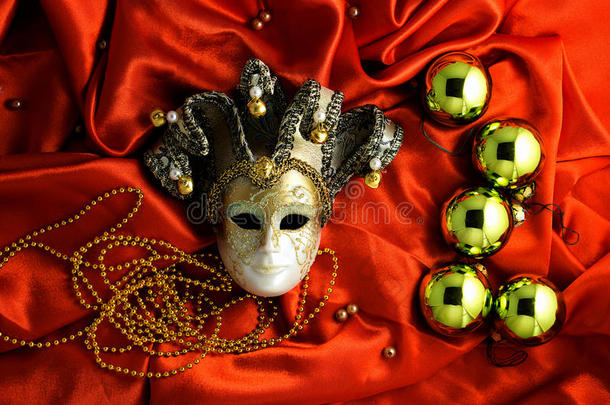 金色圣诞树球的背景，金色的装饰品和金色的面具在红色闪亮的丝绸织物上