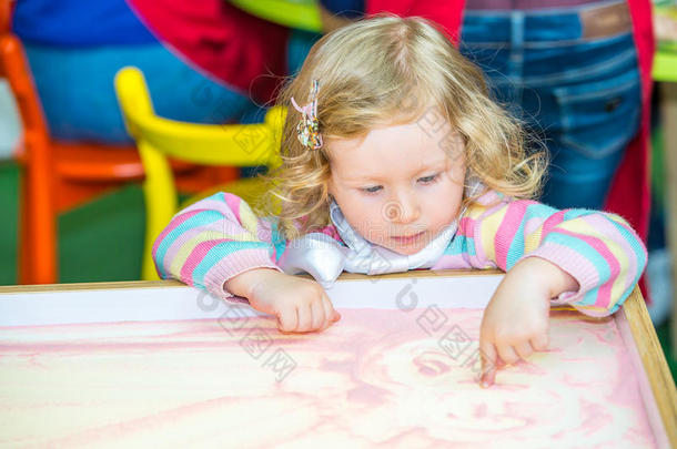 可爱的小女孩在幼儿园的桌子上画学龄前的沙子