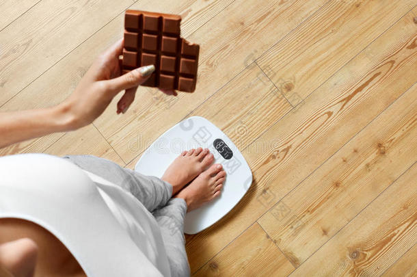 饮食。 体重秤上的女人，巧克力。 不健康的食物。 体重