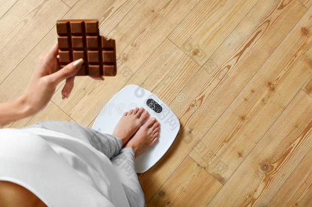 饮食。 体重秤上的女人，巧克力。 不健康的食物。 体重