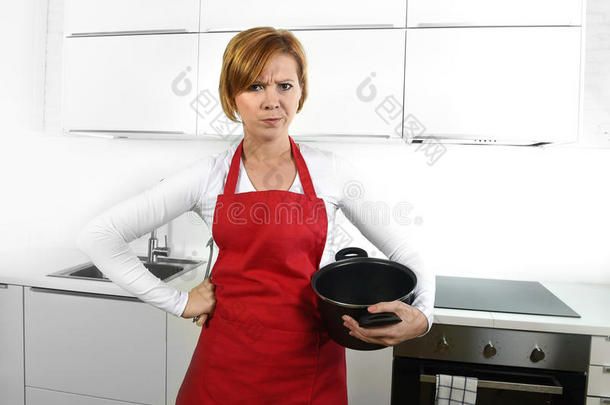 做饭的女人在愤怒，沮丧，沮丧的脸，表情在围裙，拿着烹饪锅肮脏的编辑
