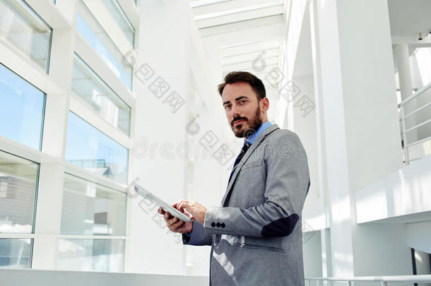 全长肖像，一个年轻的聪明的董事总经理拿着触摸垫，同时站在大白色走廊