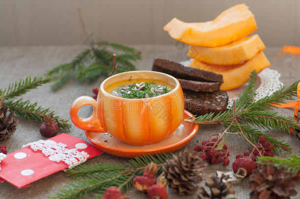 一杯橙色的南瓜汤，几片黑麦面包，新鲜南瓜和冬天装饰元素在粗糙的丁香上