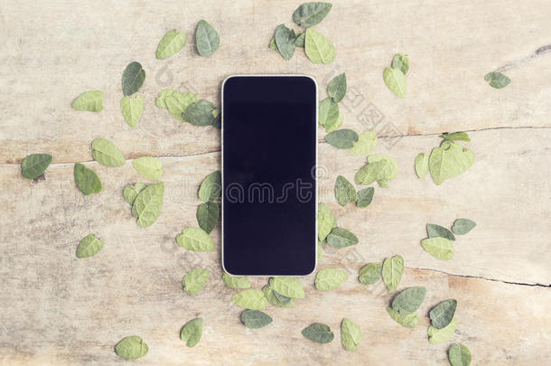 空白的黑色智能手机屏幕，木制桌子上有叶子