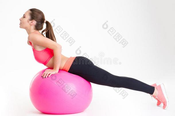 专注迷人的年轻女运动员在粉红色健身球上做伸展运动