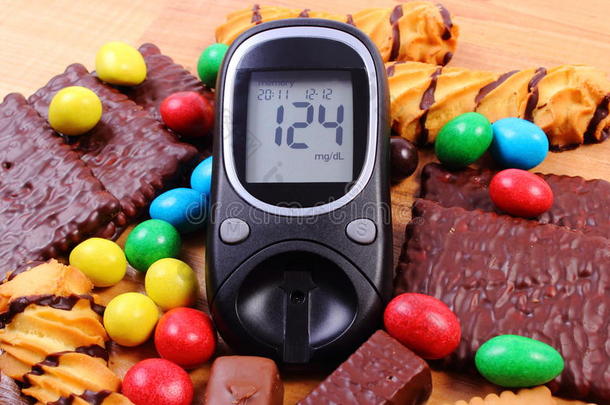 <strong>血糖仪</strong>，木制表面有一堆糖果，糖尿病和不健康的食物