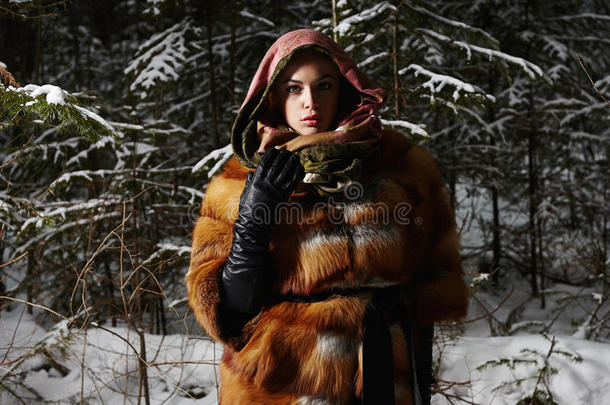夜晚冬天森林里的美女模特女孩。 穿着时尚皮毛外套和围巾的漂亮年轻女人