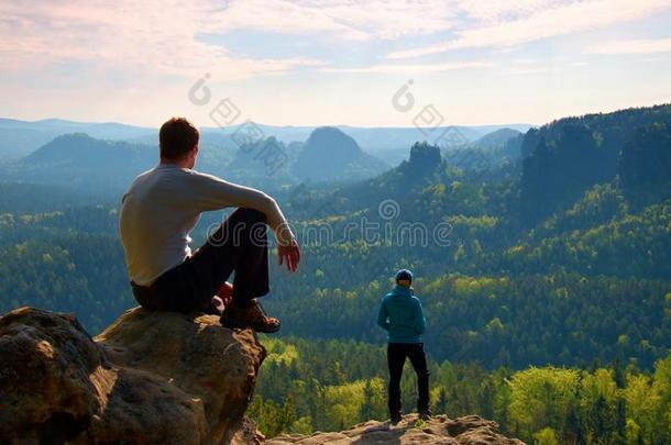 男孩和女孩的游客呆在悬崖上思考。 梦幻的雾状景观，蓝色的薄雾日出在美丽的山谷下面