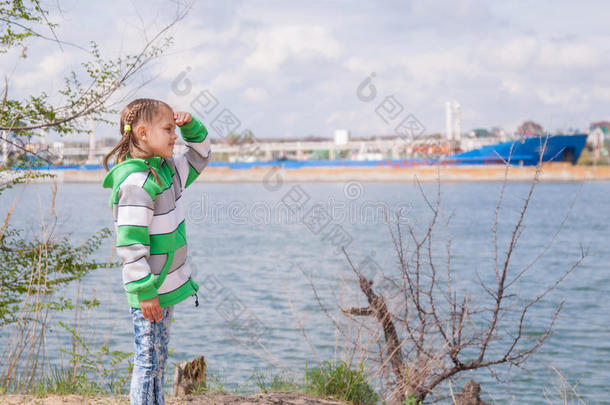 一个女孩站在漂浮的船上的河边，望着远处