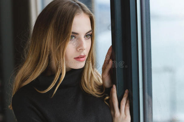 有吸引力的忧郁的年轻女人看着窗外