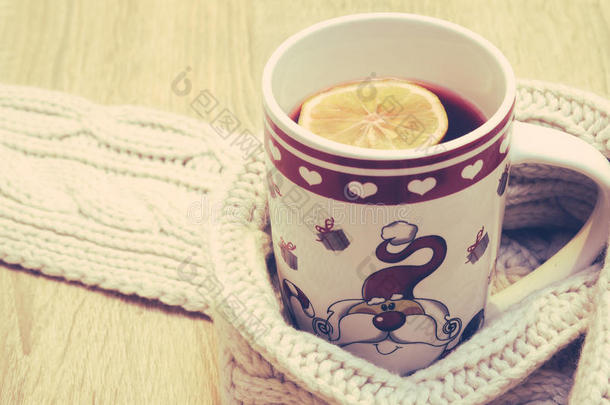 一杯加柠檬的热茶，在木制背景上戴上温暖的冬季围巾