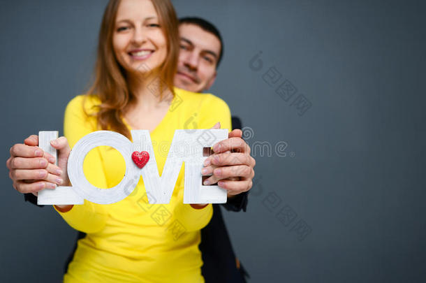 美丽的微笑的夫妇抱着爱的话语，站在灰色的背景上