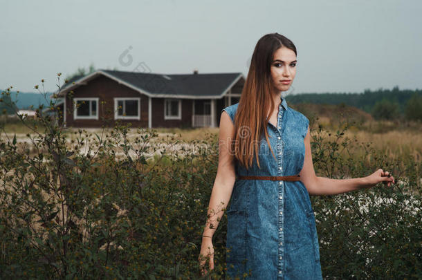 可爱的乡村女士站在高高的草地上对抗牧场的房子