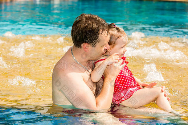 积极的父亲教他蹒跚学步的女儿在热带度假胜地的游泳池里游泳。