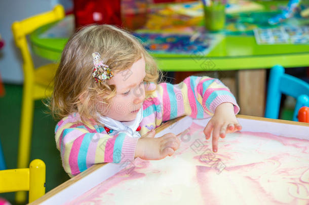 可爱的小女孩在幼儿园的桌子上画学龄前的沙子