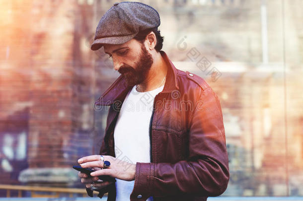 半长的肖像，一个成年留着胡须的时髦男子在手机上聊天，同时站在城市环境中