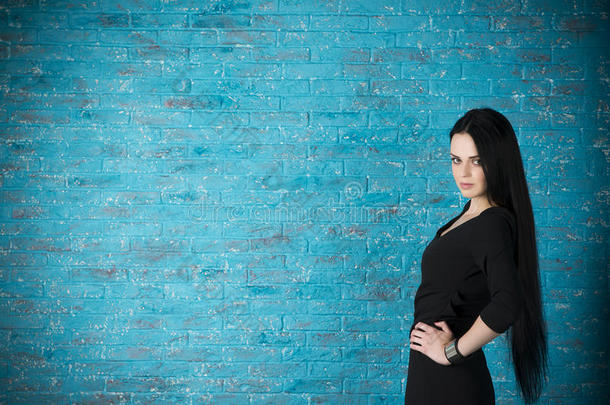 穿着黑色连衣裙的漂亮年轻女人在蓝色砖墙的背景<strong>下摆</strong>姿势