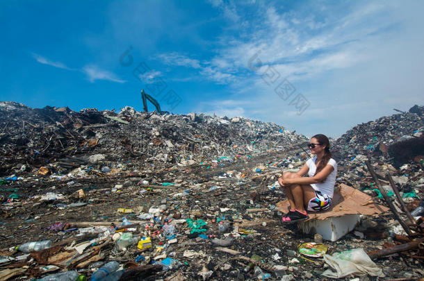 女孩坐在垃圾堆附近的路上