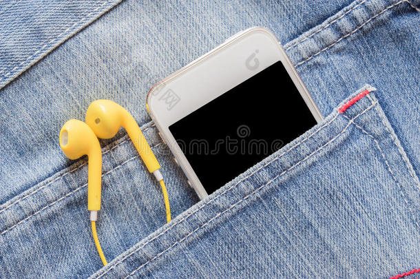 特写智能手机和黄色耳机在牛仔牛仔裤口袋。