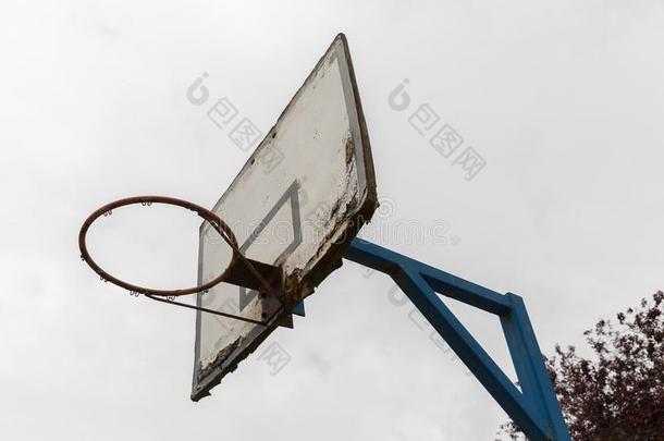 一个旧的篮球环，上面有一个白色的木板，油漆正在剥落，并固定在白色背景上的蓝色钢杆上