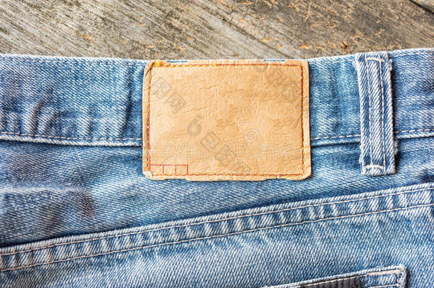 蓝色牛仔裤上的空白皮革牛仔裤标签，木制背景。
