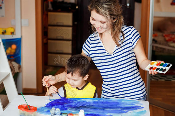 快乐的童年，小男孩和他的母亲玩耍，画画，在手掌上画画。 画一片海。