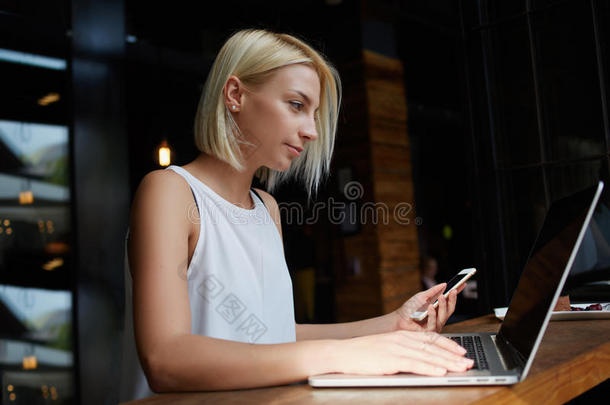 迷人的白种女人坐在现代咖啡店的室内使用手机和笔记本电脑，