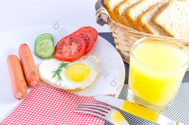 早餐在桌子上煎鸡蛋，在心形的油炸香肠，新鲜的切片蔬菜，果汁，切片不新鲜