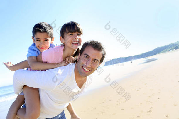 父亲背着两个孩子在海滩上