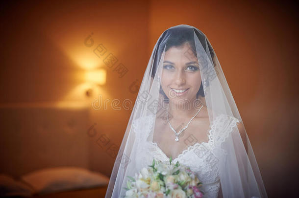 美丽的新娘手捧花束，在婚礼当天在房间里摆姿势