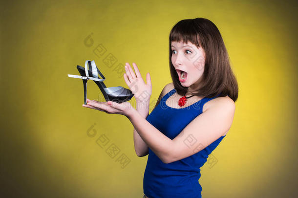 时尚女人看高跟鞋。 女人喜欢鞋子的概念。 尖叫的女孩和黄色背景的高跟鞋。