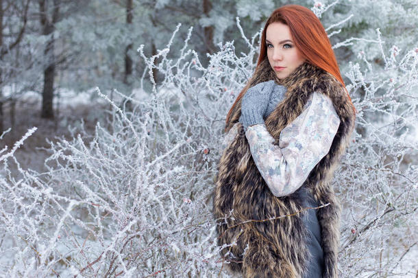 美丽可爱的年轻女孩，红头发，走在一片白雪皑皑的森林里，在树林里，错过了头三个月的红色灌木丛
