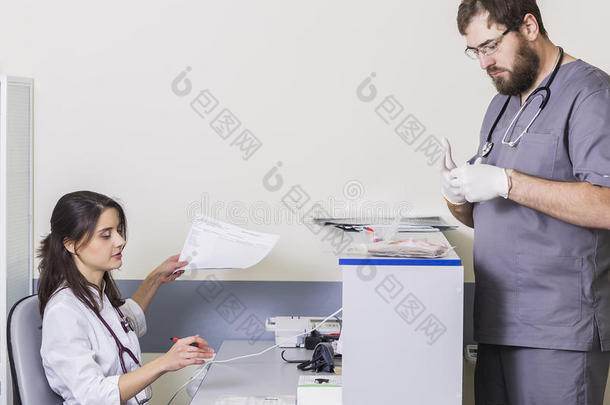 女医生坐在桌子旁，一名男医生拿着文件在<strong>医院</strong>