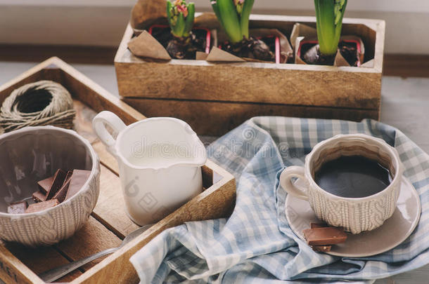 舒适的冬天早晨在家。 木制托盘上的咖啡、牛奶和巧克力。 花在背景上。 温暖的心情