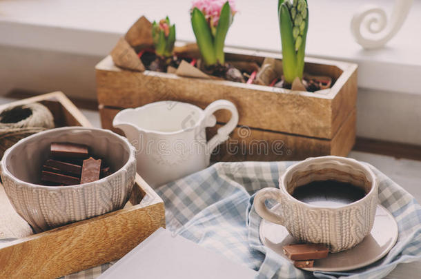 舒适的冬天或春天的早晨在家里。 木制托盘上的咖啡、牛奶和巧克力。 背景上的风信子花。 温暖的心情