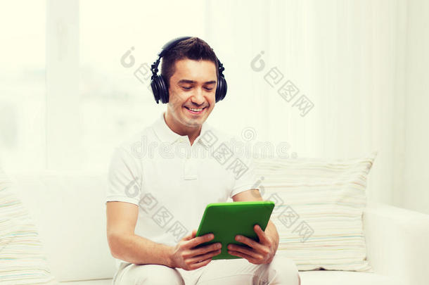 在家里带着平板电脑和耳机的微笑男人