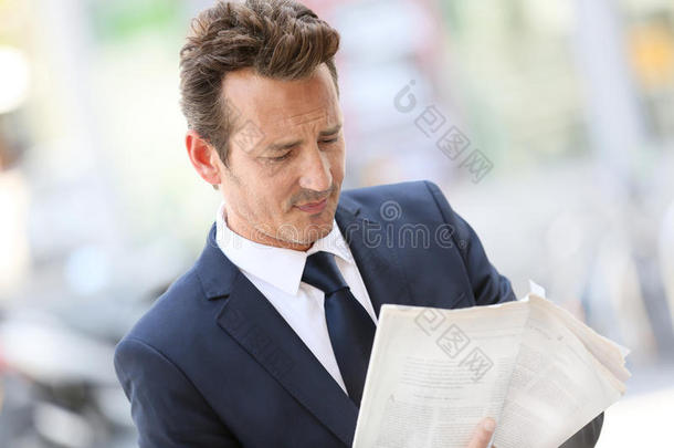 英俊的商人在街上看报纸