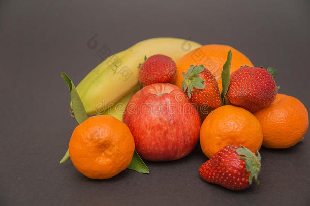香蕉，苹果，橘子，草莓和三个橘子，叶子在一个美丽的灰色背景，美丽的颜色和装饰