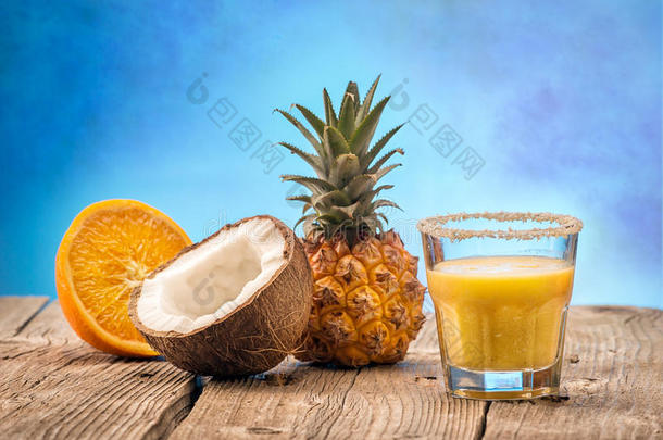 水果菠萝平滑与椰子和橙色在木桌上分离在蓝色背景