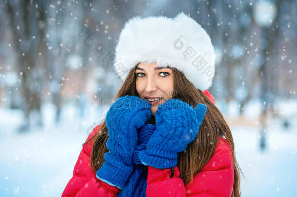 冬天雪景中年轻女子的美丽冬天肖像。 一个戴着白色毛皮帽子的女孩用手捂住脸博士