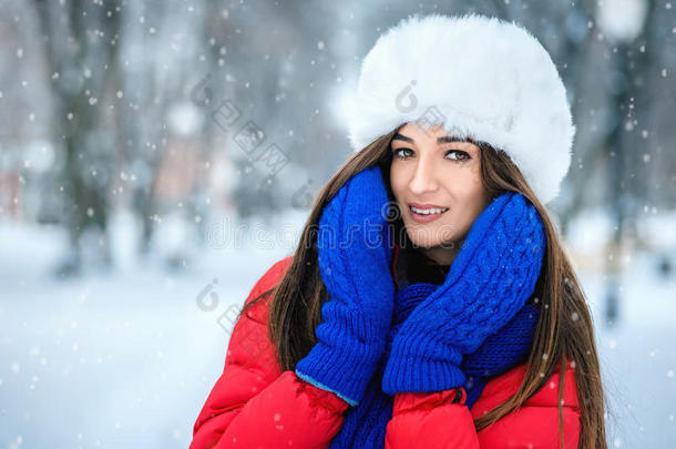 冬天雪景中年轻女子的美丽冬天肖像。 一个戴着白色毛皮帽子的女孩用手捂住脸博士