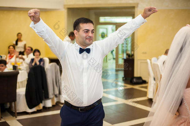 英俊快乐的新郎穿着白色衬衫，在招待会上与新娘第一次跳舞时玩得很开心
