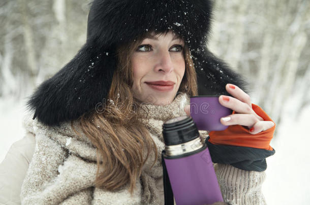 美丽的金发女孩在雪林的热水瓶里喝热茶