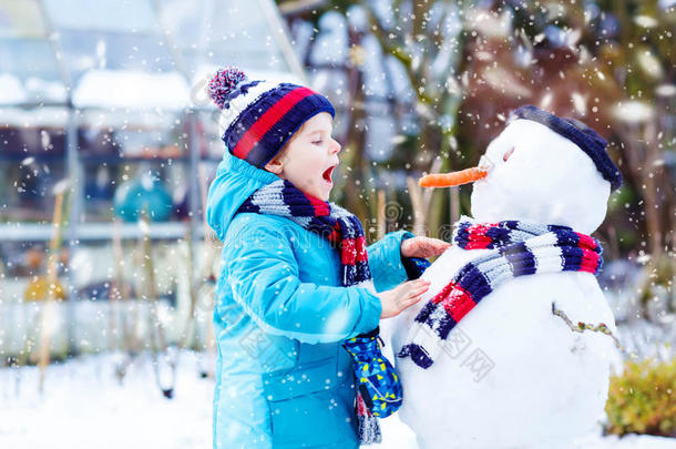 有趣的男孩穿着五颜六色的衣服在户外堆雪人