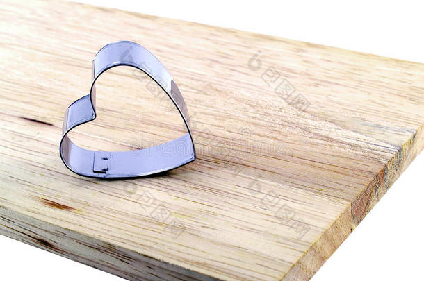 关闭单心形状的金属饼干切割机在棕色木制切割板上隔离在白色背景上