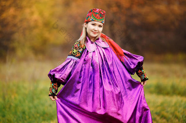漂亮的漂亮女孩穿着民族鲜艳的紫色连衣裙，头上戴着红色的头巾，装饰品和刺绣。 五颜六色的