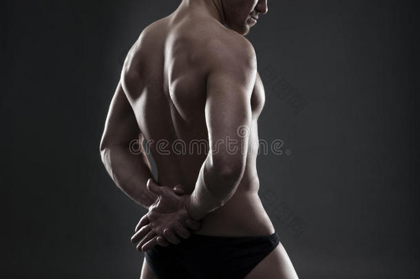 英俊的肌肉健美者在灰色背景上摆姿势。 低调的演播室镜头