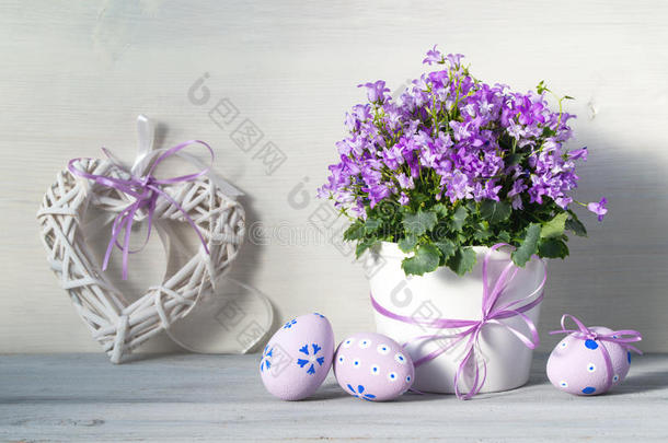 复活节装饰与复活节鸡蛋，一壶春天紫色的花和心在一个白色的木制背景