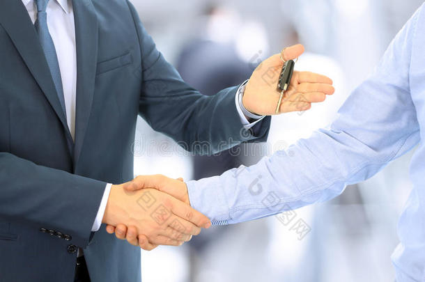 汽车推销员把一辆新车的钥匙交给一位年轻的商人。 两个商人之间的握手。 专注于一把钥匙