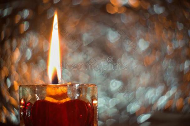 在玻璃烛台上用蜂蜡制成的燃烧蜡烛上用红色的心合上图片。